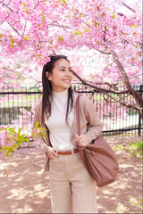 Asian woman smiling under blooming cherry blossom tree in springtime