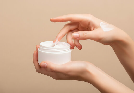 A pair of hands holding a jar of white skincare cream, one hand squeezing out a small amount of cream