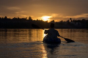 A man paddles a kayak on a tropical island with a sunset in the background. A man enjoys the sunset while playing kayak