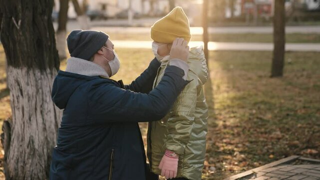 father wears kid mask on his face while walking city park, protect child's body from coronavirus infection, little daughter and dad comply with safety rules of quarantine for going out, happy family.