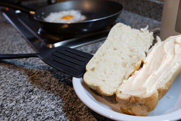 A loaf of bread cut in half and spread with plenty of mayonnaise and a frying pan with an egg...