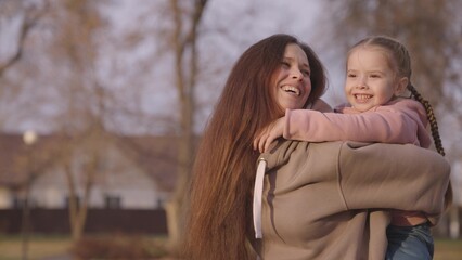 mother is circling child in her arms, cheerful kid with mom, happy family, children's dream of flying, baby smiles and laughs, parent in arms of little funny girl, beloved daughter playground day off.