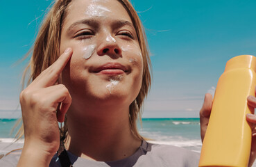 Teen applying sunscreen on face, arm, and leg under direct sun. Summer skincare, blue sky, beach background, and beige hammock. Sun protection routine, outdoor wellness