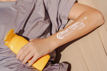 Teen applying sunscreen on face, arm, and leg under direct sun. Summer skincare, blue sky, beach background, and beige hammock. Sun protection routine, outdoor wellness