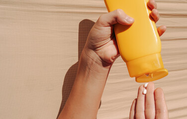 Teen applying sunscreen on face, arm, and leg under direct sun. Summer skincare, blue sky, beach background, and beige hammock. Sun protection routine, outdoor wellness
