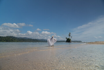 The wind blows the shawl worn by a woman standing on a tropical beach. Happy young woman wearing a shawl on the beach on a sunny day