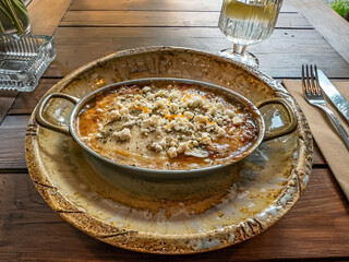 Delicious Hot Casserole with Feta Cheese Served in a Rustic Pan at an Outdoor Restaurant. Al Fresco Dining: A Hearty Baked Dish on a Wooden Table at a Summer Cafe Terrace
