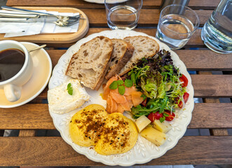 A savory breakfast served at an outdoor cafe, featuring a generous platter with benedict eggs, salmon, fresh salad, and bread.Close-up of a balanced breakfast meal on a decorative plate