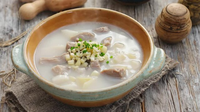 Bulgarian shkembe chorba, tripe soup served in a bowl with garlic and vinegar, rustic setting with natural light shining through a window
