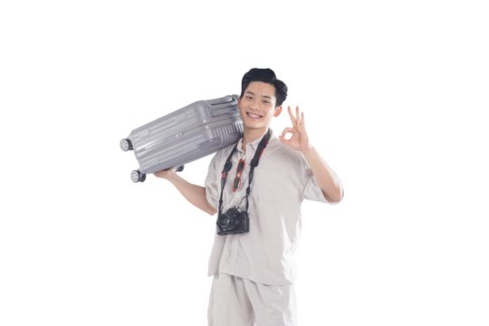 Ready for Vacation: A smiling young man, ready for adventure, carries a suitcase over his shoulder, gives an "OK" sign and holds a camera. He's dressed in light clothing, ready for a trip.