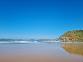 Fototapeta premium Sunny day at Geribá Beach, Búzios, Brazil. Golden sand, crystal clear water, strong waves, vibrant blue sky. Tropical paradise, serene landscape, summer vibe during Brazilian winter.
