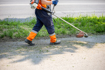 Worker trims grass along roadside with professional equipment during sunny day