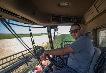 Farmer driving combine harvester in wheat field.