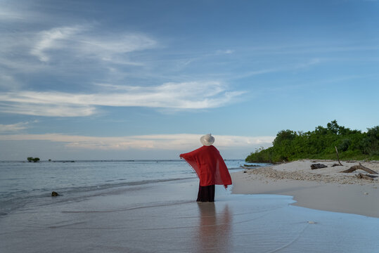The wind blows the shawl worn by a woman standing on a tropical beach. Happy young woman wearing a shawl on the beach on a sunny day