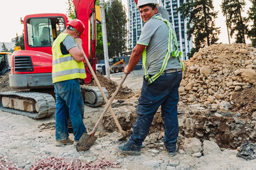 Construction workers repairing city infrastructure with heavy equipment and red polypropylene pipes. Urban utility maintenance, excavation, and roadwork in progress