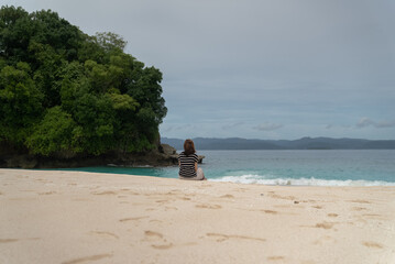 A young woman enjoys the beauty of a tropical beach. A young woman sits alone on the beach