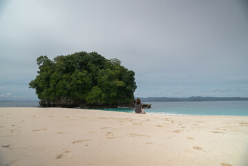 A young woman enjoys the beauty of a tropical beach. A young woman sits alone on the beach