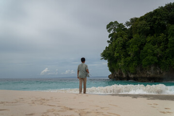 A man fishing off the coast of a tropical island. An angler uses a rod to pull a fish from the choppy shoreline and turquoise water