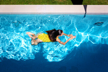 Woman in yellow swimsuit swimming in the pool on a summer day
