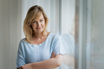Shot of a blond haired woman standing by the window