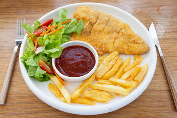 Fish steak with vegetable salad and french fries on a plate, top view