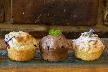 Three different flavours (blueberry, chocolate-mint and rosemary) of homemade muffins against a rustic brown background.
