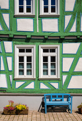 Facade of half timbered house and blue bench in Idstein Germany. Green and white wall and truss with windows of a medieval old house. Idstein is a idyllic small town near Frankfurt.