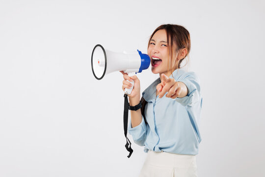 A happy young Asian woman points with her finger on camera, shouting into megaphone to announce news. She is excited to speak through this speaker, a clear megaphone. isolated studio white background