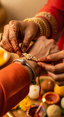Raksha Bandhan 2025 &ndash; Close up of hands tying designer rakhi during sacred ritual with festive lights, sweets, and love-filled cultural ambiance