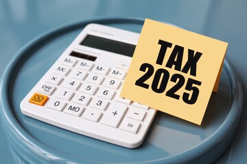A calculator with a yellow sticky note on top that says tax 2025 on a blue round surface