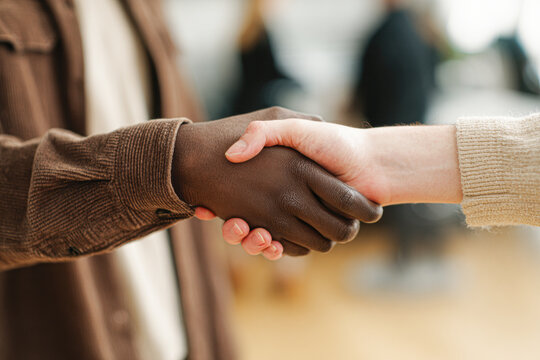Two people of different skin tones shaking hands, symbolizing unity, trust, and cooperation in a blurred indoor setting.
