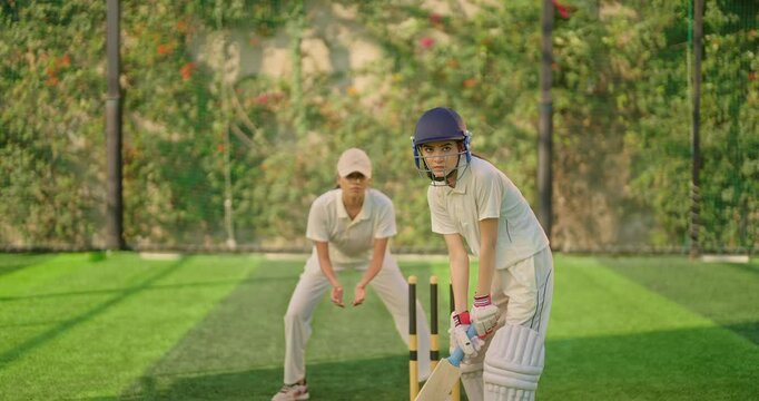 Indian gen z young adult athlete sports woman girl standing at outdoor match play ground wear gloves white uniform protective helmet asian cricket player female lady hold bat hitting ball do practice	