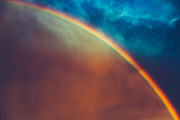 A beautiful huge rainbow displays a colorful arc across the dramatic blue sky. A vibrant rainbow...