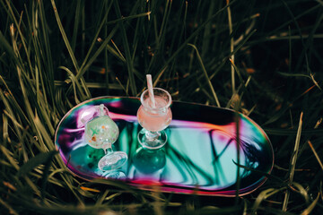Two refreshing cocktails on a tray, resting on a bed of green grass. Colorful cocktails with straws...
