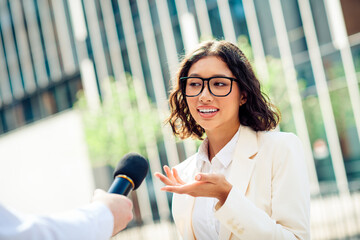 Confident young businesswoman giving an interview in sunlight in the modern urban setting,...