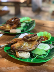 Ayam Tempong, Indonesian fried chicken served with rice, sambal, fresh vegetables, and tofu on banana leaf-lined plates, offering a traditional and spicy culinary experience.
