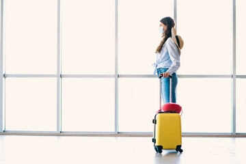 Passenger woman with yellow suitcase waiting in airport terminal, wearing casual clothes and face...