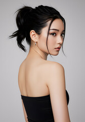 Fototapeta premium A beautiful young asian woman with long black hair in a ponytail looks over her shoulder wearing a black top