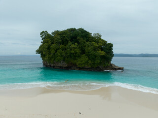 An aerial view of a tropical island with white sand beaches and turquoise waters. Waves crashing on a white sandy tropical beach