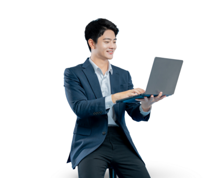 A happy young Asian professional sits on a stool, smiling as he works or browses on his laptop computer. Isolated on a PNG background.