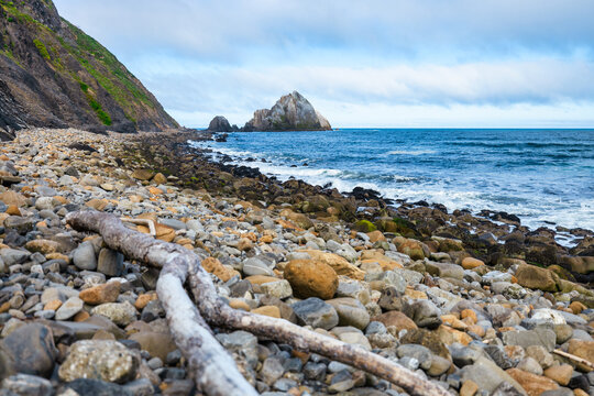 Close-up view of San Pedro Rock near Pacifica, California. Layered volcanic formations rise from the ocean, surrounded by tidepools and rocky shores under a dramatic cloudy sky