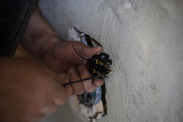 An electrician uses a screwdriver to connect wires to a socket during electrical installation or repair work on a concrete wall. The electrician installs the socket by securing the wires.