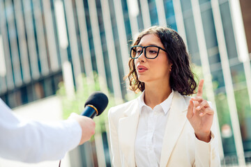 Confident businesswoman being interviewed outdoors in a modern urban setting on a sunny day,...