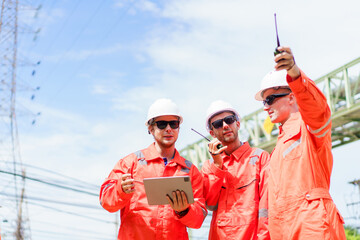 Engineering team in safety gear planning pipeline maintenance at oil and gas refinery site with storage tanks in the background.