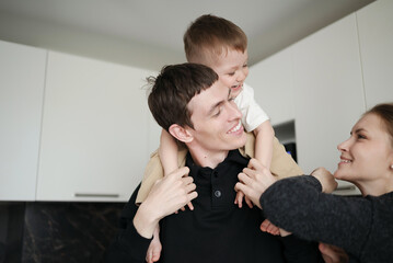 Happy father carrying his laughing son on his shoulders while smiling mother stands nearby in a...