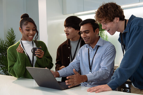 A diverse group of four young adults engaging with a laptop, showcasing collaboration and excitement in a modern workspace. - Powered by Adobe