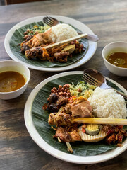 Nasi Campur is a Traditional Balinese rice dish served on a banana leaf with various side dishes,...