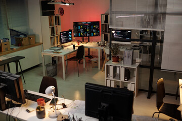 Empty modern office with multiple computer monitors displaying code and data, desks arranged in open workspace, suggesting scam call center environment with technology setup