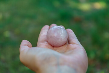 A hand gently cradles a smooth, polished sphere of rose quartz, showcasing its delicate pink hue...