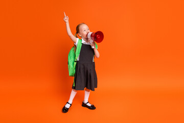 Young schoolgirl in uniform with a backpack using a red megaphone while pointing up against an...